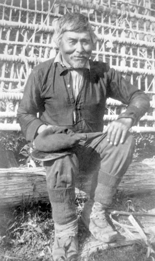Old Enoch; was the builder of all fish traps; in the background is one he has just completed, made from young Jack pine and lashed together with wild rose roots.